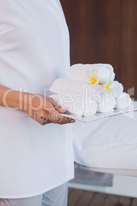 Mid section of masseur holding rolled up towels