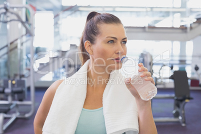 Fit brunette drinking water with towel around shoulders