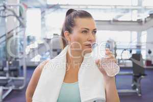 Fit brunette drinking water with towel around shoulders