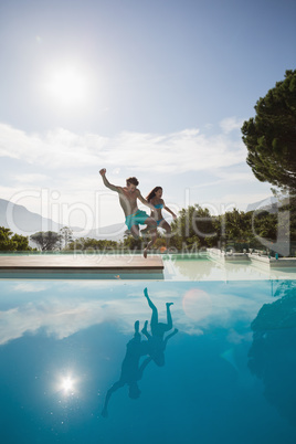 Cheerful couple jumping into swimming pool