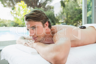 Handsome man receiving stone massage at spa center