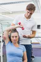 Personal trainer helping client lift dumbbell