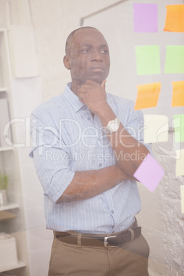 Thoughtful businessman looking at sticky notes on window