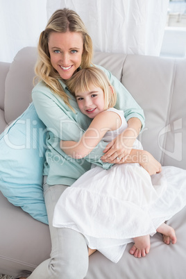 Mother sitting on the couch with her daughter smiling at camera
