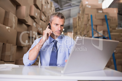 Warehouse manager using cellphone and laptop