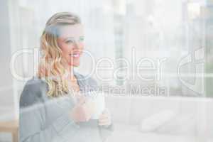 Smiling blonde woman holding mug of coffee looking away