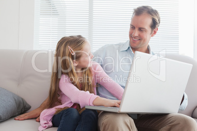 Casual father and daughter using laptop on the couch