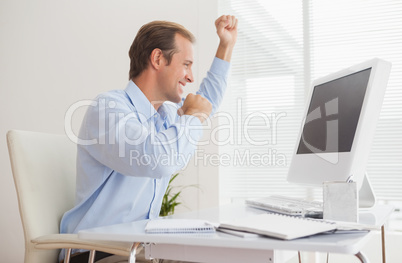 Casual businessman cheering at his desk