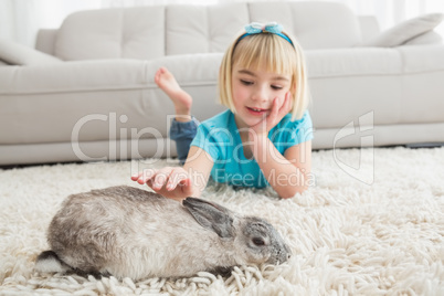 Little girl lying on rug stroking the rabbit
