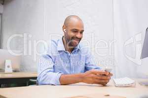 Businessman listening music with mobile phone at desk