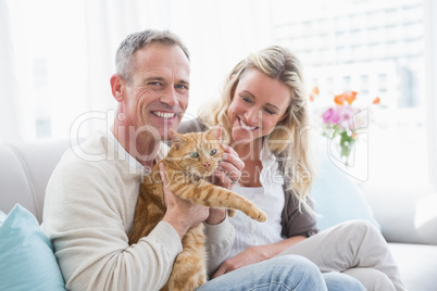 Smiling couple petting their gringer cat on the couch