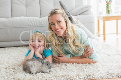 Smiling daughter and mother laying on the floor with rabbit