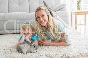 Smiling daughter and mother laying on the floor with rabbit