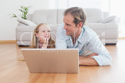 Casual father and daughter using laptop on the floor