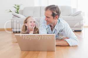 Casual father and daughter using laptop on the floor