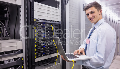 Smiling technician using laptop while analysing server