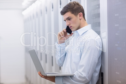 Young technician phoning and using his notebook