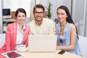 Smiling business team using laptop and having coffee