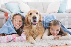 Sisters lying on rug with golden retriever under a blanket