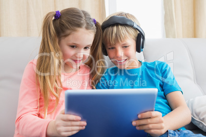 Happy siblings using tablet pc on sofa