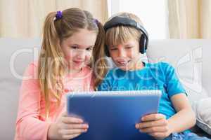 Happy siblings using tablet pc on sofa