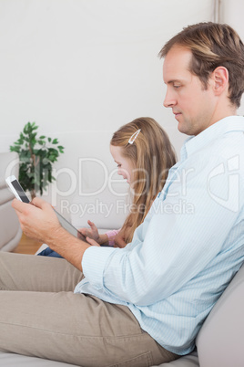 Casual father and daughter using tablet and smartphone on the co