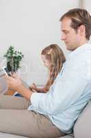 Casual father and daughter using tablet and smartphone on the co