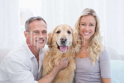 Smiling couple petting their golden retriever on the couch