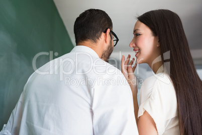 Businesswoman whispering into male colleagues ear