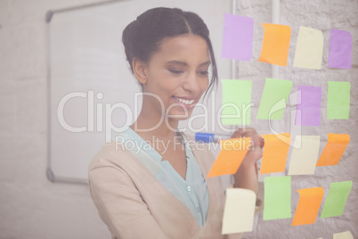 Smiling businesswoman writing on sticky notes on window