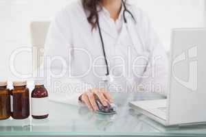 Doctor using laptop near pill bottles