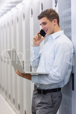 Smiling technician phoning and using his notebook