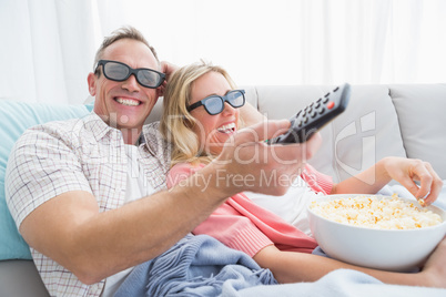 Happy couple wearing 3d glasses eating popcorn