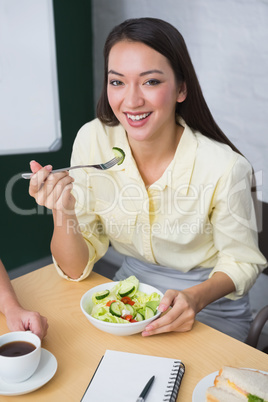 Smiling pretty businesswoman eating healthy salad