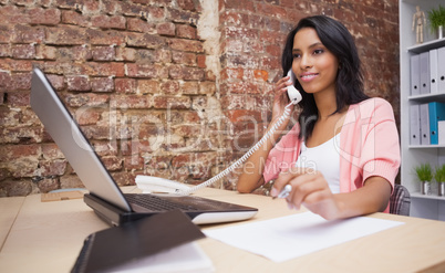 Woman calling and using laptop sitting at her desk