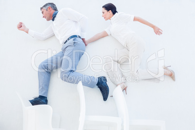 Business partners jumping over chairs