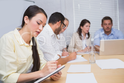 Woman taking notes while colleagues are talking behind her