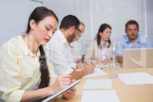 Woman taking notes while colleagues are talking behind her