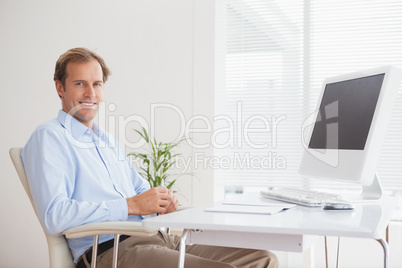 Casual businessman smiling at camera at his desk