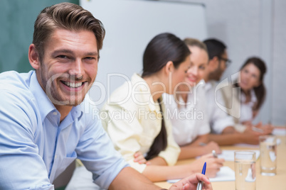 Business man smiling at camera with team behind him