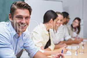 Business man smiling at camera with team behind him