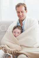 Father and son wrapped in a blanket on the couch