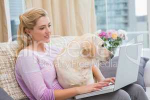 Beautiful blonde using laptop on couch with pet dog
