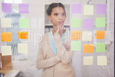 Creative businesswoman looking at sticky notes on window