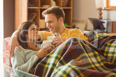 Young couple cuddling on the couch under blanket