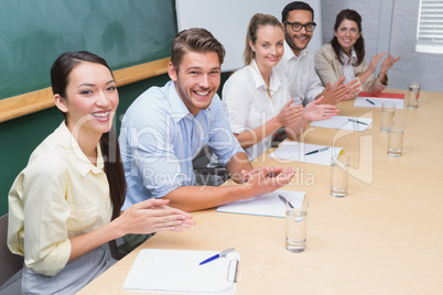 Business team sitting in a row clapping at camera