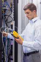 Focused technician using digital cable analyser on servers