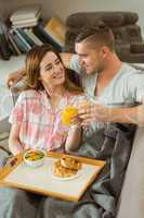 Cute couple relaxing on couch with breakfast