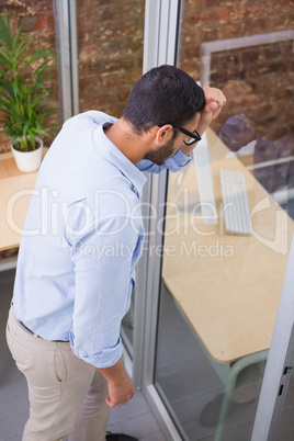 Thoughtful businessman standing against glass wall at office