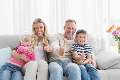 Happy family sitting on sofa giving thumbs up